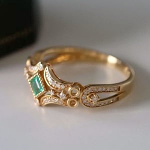 May include: A gold ring with a green emerald gemstone and small diamonds set in a delicate, ornate design.