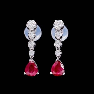 Puede incluir: Un par de pendientes de plata con una piedra preciosa de rubí en forma de pera y una fila de pequeños diamantes redondos.