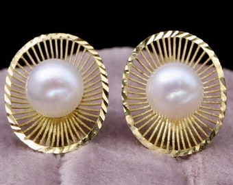 May include: A pair of gold earrings with a pearl in the center of each. The earrings are round and have a sunburst design.