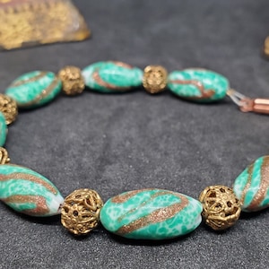 May include: A green and gold bracelet with oval-shaped beads. The beads are green with gold swirls and are separated by gold metal beads.