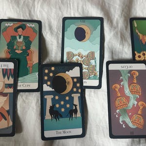 Könnte beinhalten: Ein Tarotkarten-Spread mit zehn Karten, darunter Die Hohepriesterin, Der Mond, Acht der Kelche und Drei der Stäbe. Die Karten liegen auf einer weißen Stoffoberfläche.