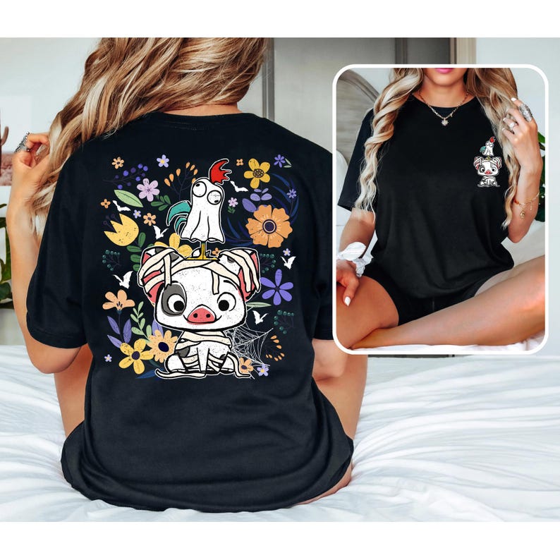 May include: Black t-shirt featuring a colorful graphic of a cartoon pig wrapped in bandages, a ghost, and a rooster, surrounded by flowers and a spiderweb. A smaller version of the graphic is on the front. The shirt is a casual wear item.