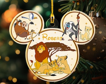 Puede incluir: Un adorno navideño blanco, dorado y marrón con forma de cabeza de Mickey Mouse. El adorno presenta personajes de El Rey León, incluyendo Simba, Nala y Mufasa. El adorno está personalizado con el nombre "Robert".