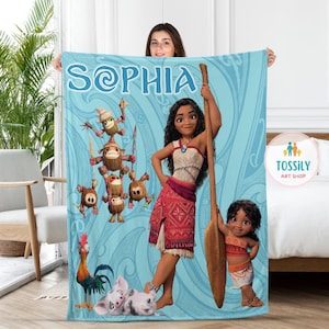 Puede incluir: Una manta de franela azul con un dise&ntilde;o polinesio que presenta a Moana y sus amigos. La manta tiene el nombre "Sophia" escrito en una fuente decorativa.