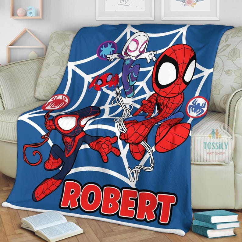 K&ouml;nnte beinhalten: Eine blaue Fleece-Decke mit einem wei&szlig;en Spinnennetz-Design. Die Decke zeigt vier Comic-Spider-Man-Charaktere, darunter Spider-Man, Spider-Gwen und Miles Morales. Die Decke ist mit dem Namen "ROBERT" personalisiert.