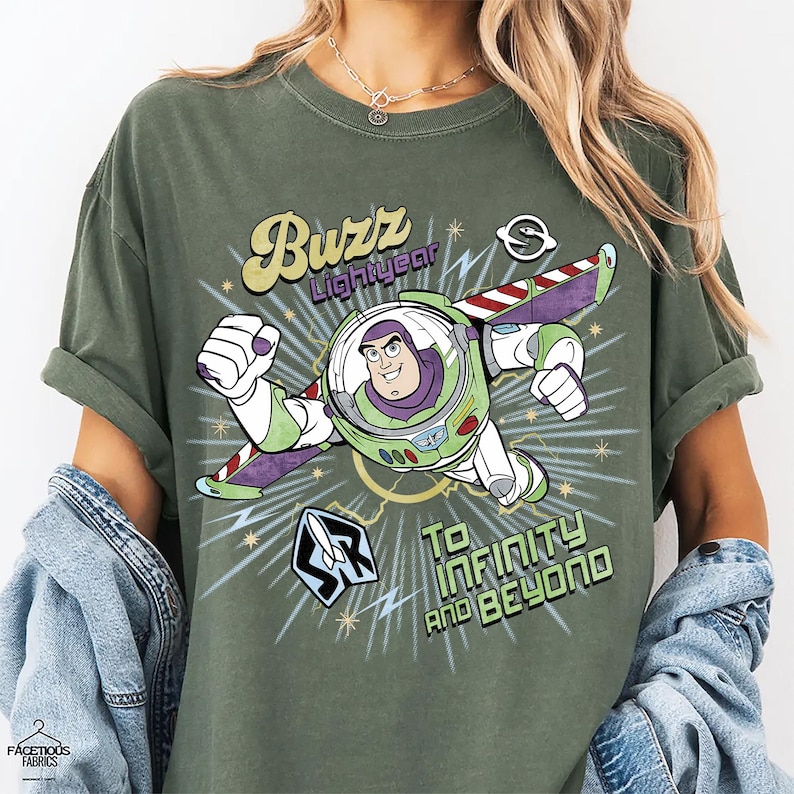 Puede incluir: Camiseta verde oliva con un gr&aacute;fico de Buzz Lightyear en vuelo, con el texto "Buzz Lightyear" arriba y "To Infinity and Beyond" abajo. El dise&ntilde;o incluye acentos verdes, morados, blancos y amarillos.