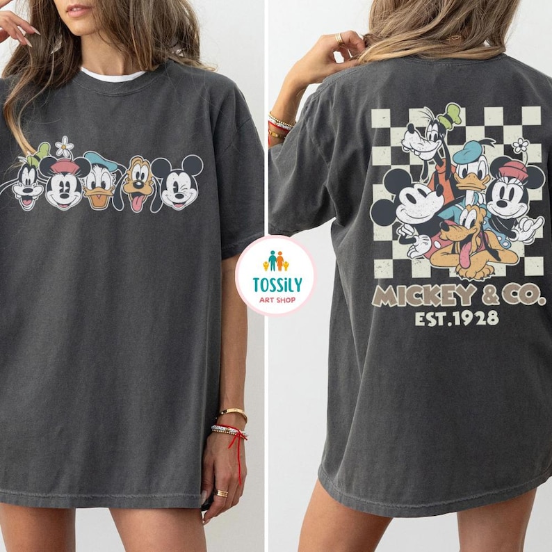 May include: Dark gray t-shirt featuring a classic cartoon character design. The front displays a row of characters, while the back showcases a checkered pattern with more characters and the text "Mickey & Co. EST.1928".