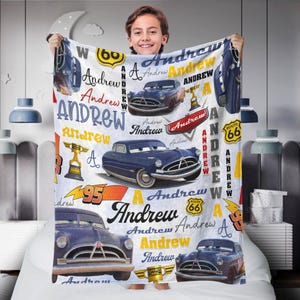 May include: A personalized blanket featuring the name "Andrew" in various fonts and colors, along with images of a blue vintage car, trophies, and Route 66 signs. The blanket is white with a soft texture.