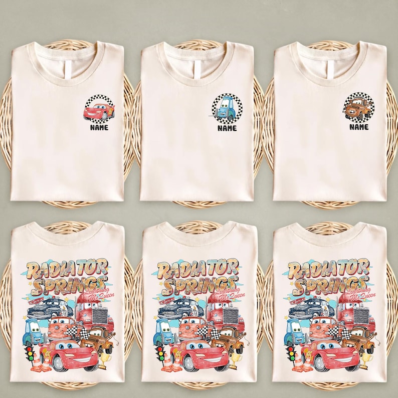 Puede incluir: Seis camisetas de color crema. La fila superior presenta peque&ntilde;os gr&aacute;ficos de coches con la palabra "NAME" debajo. La fila inferior muestra un gr&aacute;fico m&aacute;s grande con el texto "RADIATOR SPRINGS" y varios personajes de coches. Las camisetas est&aacute;n dispuestas sobre esteras tejidas.
