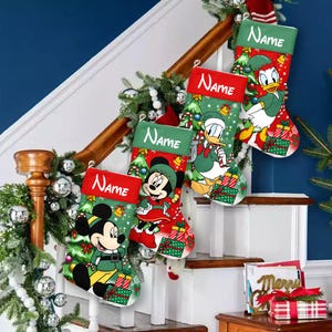 May include: Four Christmas stockings with Disney characters Mickey Mouse, Minnie Mouse, and Donald Duck. Each stocking has a red cuff with the word "Name" in white. The stockings are decorated with Christmas trees, presents, and bells. The stockings are hanging on a staircase.