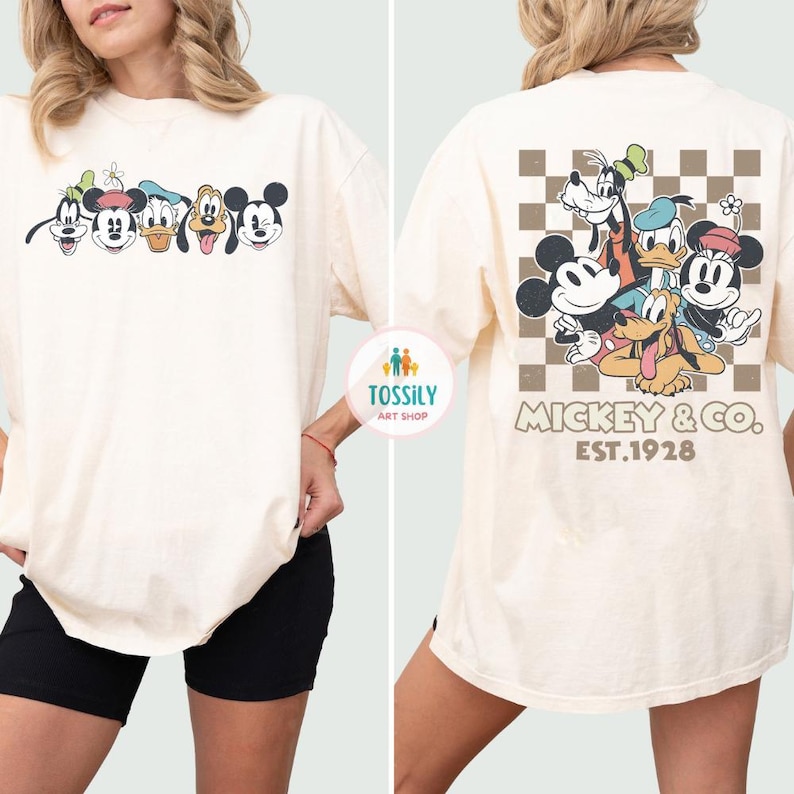 May include: Cream-colored t-shirt featuring a graphic of Mickey Mouse, Goofy, Donald Duck, and other Disney characters. The back of the shirt has a checkered pattern with the text "Mickey & Co. EST.1928".
