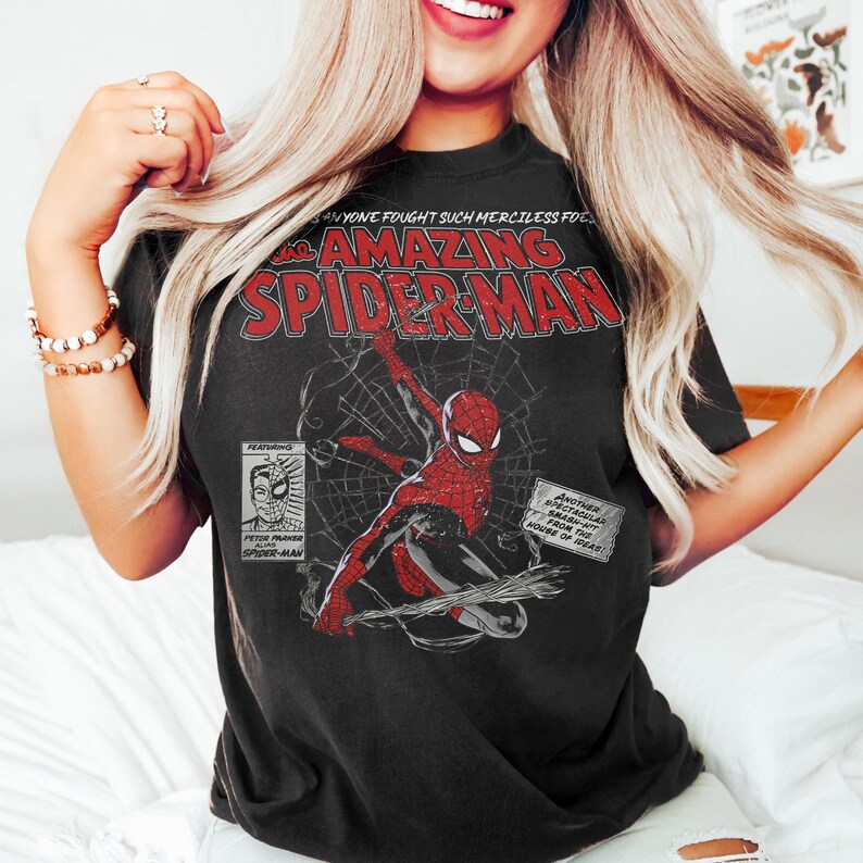 Pu&ograve; includere: T-shirt nera con una grafica a fumetti di Spider-Man in rosso e nero, con la scritta "The Amazing Spider-Man". Il design include anche il testo "Anyone fought such merciless foe" e "Another spectacular smash-hit from the house of ideas!"