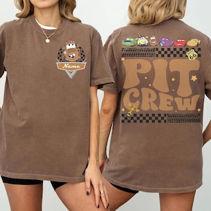May include: Brown t-shirt featuring a cartoon image of Mater from the movie Cars on the front, with the name "Name" below. The back of the shirt has the words "PIT CREW" in large brown letters, with images of other Cars characters and Route 66.