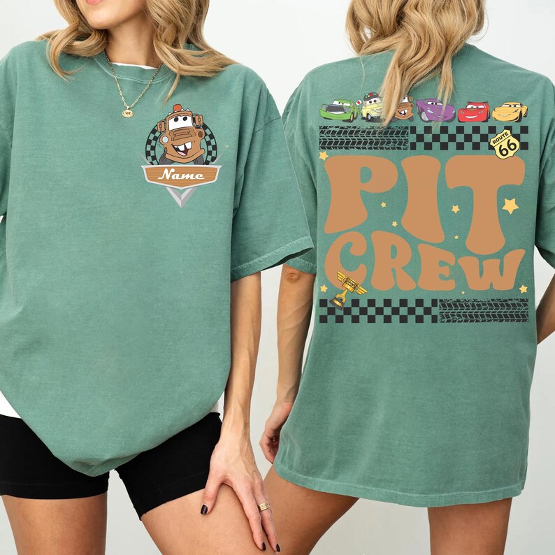 May include: A seafoam green t-shirt featuring a cartoon image of Mater from the movie Cars, with the text "Name" on the front. The back of the shirt displays the words "Pit Crew" in brown, along with various car graphics and Route 66 signage.