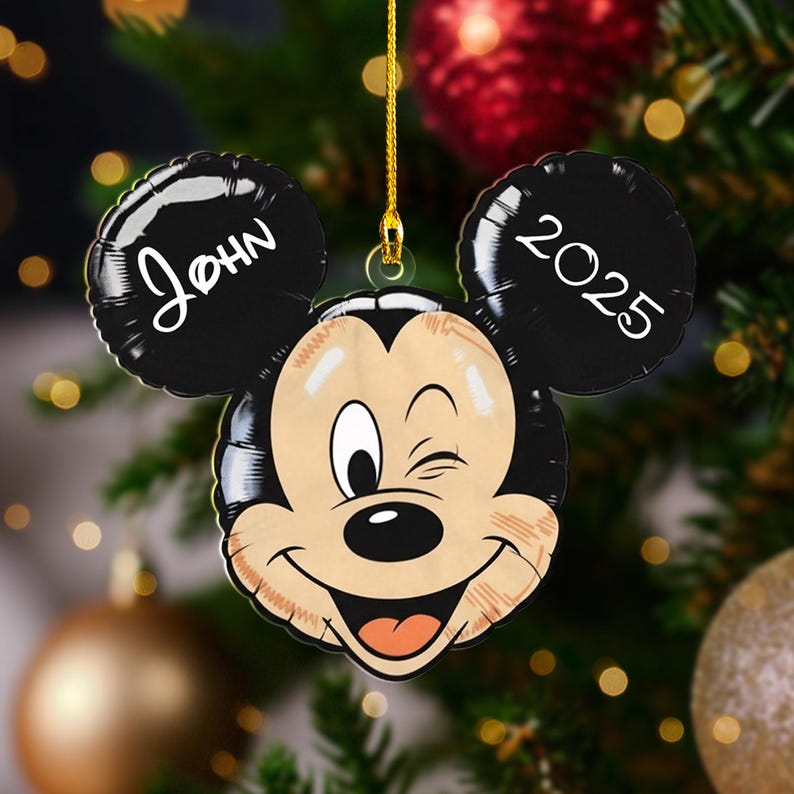 May include: A Mickey Mouse-shaped Christmas ornament with the name "John" on one ear and the year "2025" on the other. The ornament is smiling and winking, with a gold string for hanging.