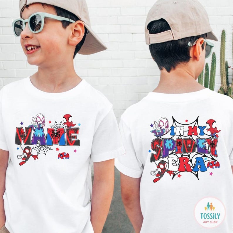 K&ouml;nnte beinhalten: Wei&szlig;e T-Shirts mit farbenfrohen Spider-Man-Grafiken. Auf einem Shirt steht das Wort "NAME" im Comic-Stil, auf dem anderen "IN MY SPIDEY ERA". Beide Shirts zeigen Spider-Man-Charaktere und Spinnennetze.