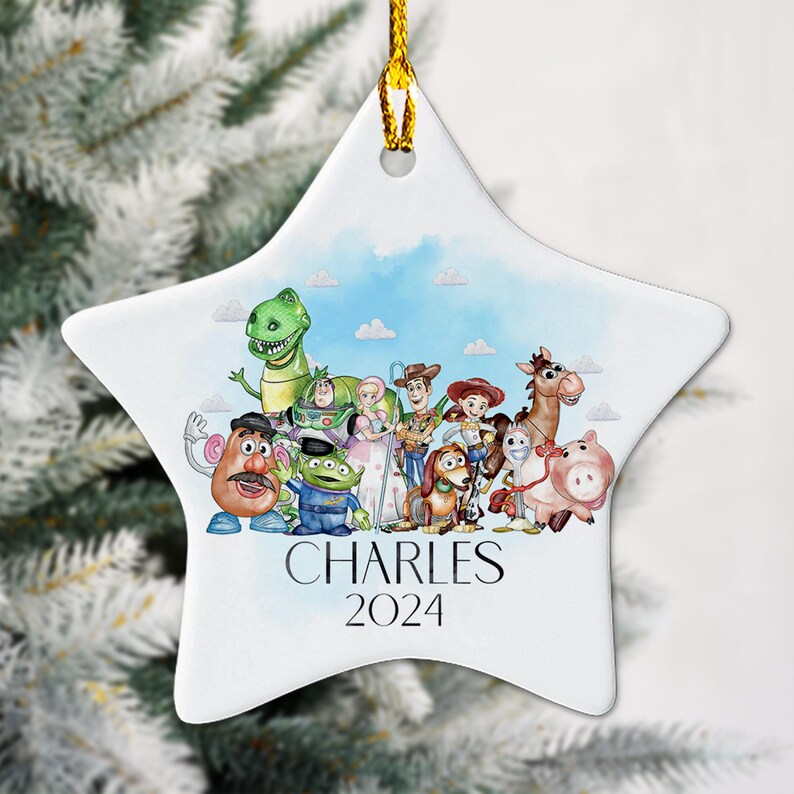 May include: A white ceramic star-shaped Christmas bauble featuring a watercolour illustration of characters from the Toy Story film franchise. The bauble depicts Woody, Buzz Lightyear, Jessie, Rex, Mr. Potato Head, Slinky Dog, and others. The bauble is personalised with the name "CHARLES" and the year "2024".