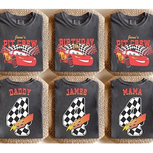 May include: Six dark gray t-shirts with various designs. Two shirts say "Jane's PIT CREW" with a red race car and checkered flag. Another says "BIRTHDAY Boy" with the same design. The other shirts say "DADDY", "JAMES", and "MAMA" with a number 4 and a checkered flag.