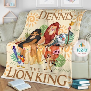 May include: A cream-colored fleece blanket with a colorful illustration of characters from The Lion King. The blanket features the text "Dennis The Lion King" and a small logo for "Tossily Art Shop".