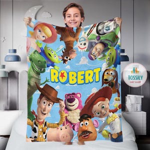 以下が含まれることがあります： トイストーリーをテーマにした青と緑のフリースブランケット。ブランケットには、ウッディ、バズ・ライトイヤー、ミスター・ポテトヘッドなどのキャラクターが描かれています。ブランケットには「ROBERT」という名前が黄色の文字で印刷されています。