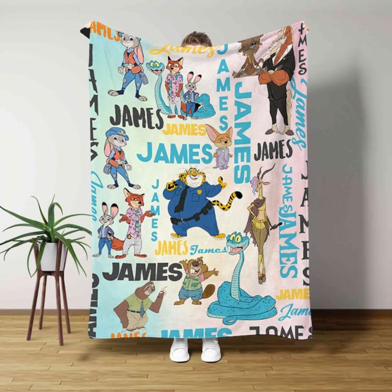 K&ouml;nnte beinhalten: Eine farbenfrohe Decke mit Zeichentrickfiguren und dem Namen "JAMES" in einem sich wiederholenden Muster. Die Decke hat einen hellblauen, rosa- und gelbfarbenen Hintergrund mit verschiedenen Tierfiguren in unterschiedlichen Outfits. Das Wort "JAMES" ist in gro&szlig;en, fetten Buchstaben geschrieben.