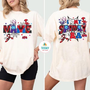 K&ouml;nnte beinhalten: Cremefarbenes T-Shirt mit einem farbenfrohen Grafikdesign. Auf der Vorderseite steht das Wort "NAME" im Comic-Stil, mit Spinnennetz- und Charakterillustrationen. Auf der R&uuml;ckseite steht "IN MY SPIDEY ERA" mit &auml;hnlichen Grafiken.