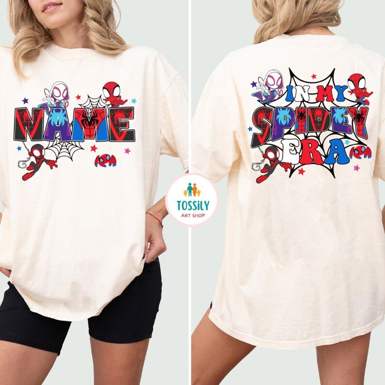 K&ouml;nnte beinhalten: Cremefarbenes T-Shirt mit einem farbenfrohen Grafikdesign. Auf der Vorderseite steht das Wort "NAME" im Comic-Stil, mit Spinnennetz- und Charakterillustrationen. Auf der R&uuml;ckseite steht "IN MY SPIDEY ERA" mit &auml;hnlichen Grafiken.