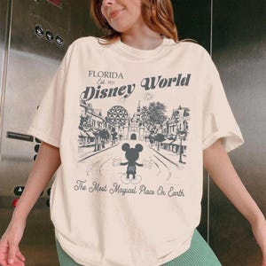 May include: Cream-coloured t-shirt with a black and white illustration of Disney World in Florida. The design includes Mickey Mouse, the text "Florida Est. 1971 Disney World," and the phrase "The Most Magical Place On Earth."
