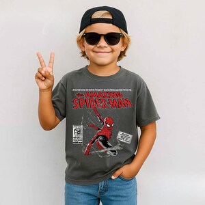 Pu&ograve; includere: Una maglietta grigio antracite con Spider-Man. La grafica include il personaggio in una posa dinamica, in stile fumetto, con la scritta "NEVER HAS ANYONE FOUGHT SUCH MERCILESS FOES AS... THE AMAZING SPIDER-MAN".