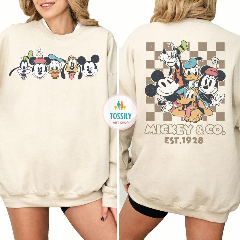 May include: Cream-colored sweatshirt featuring a cartoon graphic of Mickey Mouse, Goofy, Donald Duck, and Pluto. The front displays the characters' faces, while the back showcases a group image with a checkered background and the text "Mickey & Co. EST.1928."