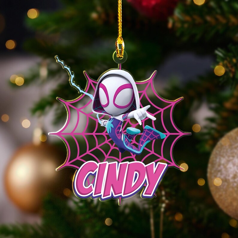 May include: A Christmas tree ornament featuring a cartoon character in a Spider-Gwen costume. The ornament is white, pink, and blue, with the name "CINDY" in pink and white. The character is posed on a pink spiderweb.