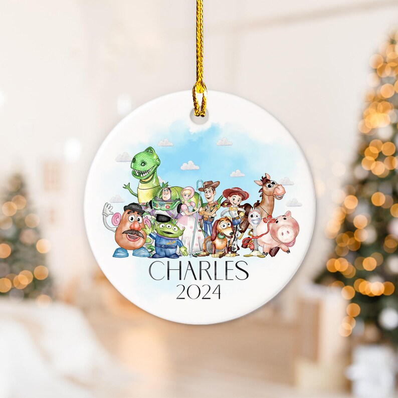 May include: A white ceramic Christmas bauble featuring a watercolour illustration of the Toy Story characters, including Woody, Buzz Lightyear, Jessie, Rex, and Mr. Potato Head. The bauble is personalised with the name "CHARLES" and the year "2024".