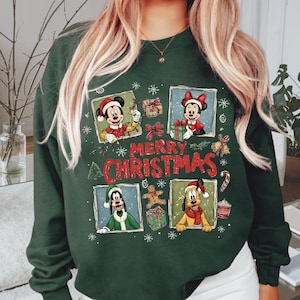 May include: Dark green sweatshirt featuring Mickey Mouse, Minnie Mouse, Goofy, and Pluto in Christmas attire. The design includes the text "MERRY CHRISTMAS" with snowflakes and festive graphics. The sweatshirt is a crew neck style.