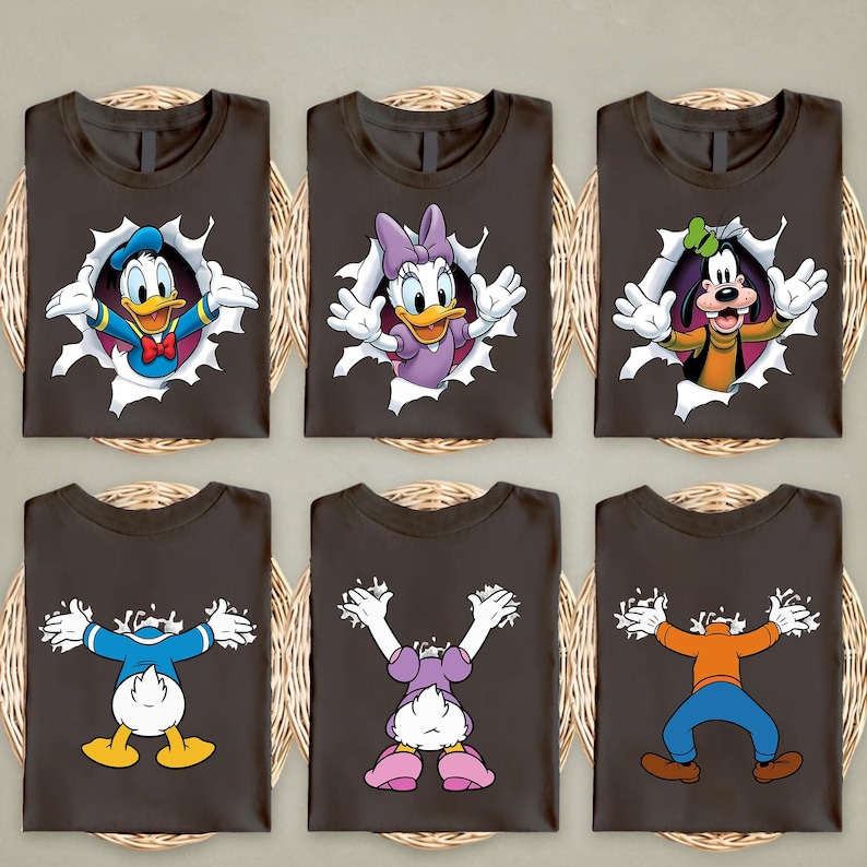 May include: Six dark brown t-shirts with cartoon character graphics. Donald Duck, Daisy Duck, and Goofy are featured, each appearing to burst through a hole. The shirts are arranged on a woven surface.