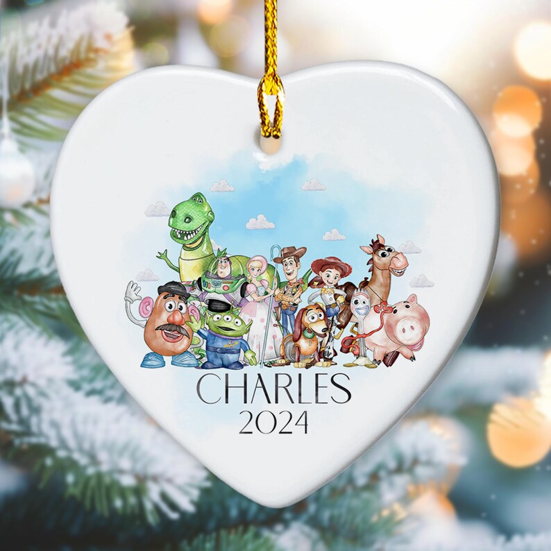 May include: White heart-shaped ceramic ornament featuring a watercolour illustration of the Toy Story characters. The characters include Woody, Buzz Lightyear, Jessie, Rex, Slinky Dog, Mr. and Mrs. Potato Head, and Hamm. The ornament is personalised with the name "CHARLES" and the year "2024".