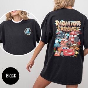 Puede incluir: Camiseta negra con un peque&ntilde;o gr&aacute;fico de coche de dibujos animados en la parte delantera y un gr&aacute;fico m&aacute;s grande en la parte trasera con el texto "Radiator Springs" y varios coches de dibujos animados. La camiseta tiene cuello redondo y mangas cortas.