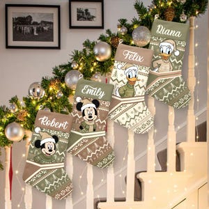 May include: Five Christmas stockings hang on a staircase, each with a different name: Robert, Emily, Felix, Diana. The stockings feature cartoon characters Mickey Mouse and Donald Duck, wearing winter attire. The stockings have a green and brown color scheme with a festive pattern.