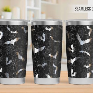 Pu&ograve; includere: Tre bicchieri in acciaio inossidabile con un design senza cuciture di pipistrelli argentati e ragnatele bianche su sfondo nero. Ogni bicchiere ha un coperchio trasparente e una base argentata, con un motivo ripetitivo di pipistrelli e ragnatele.