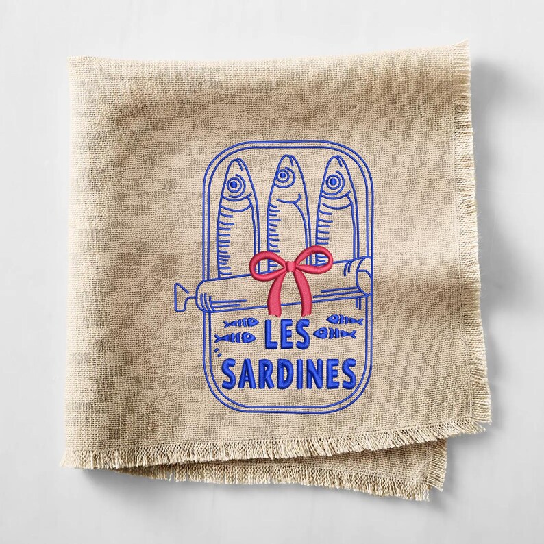 Peut inclure: Une serviette carr&eacute;e en lin beige aux bords effiloch&eacute;s pr&eacute;sentant une broderie de trois sardines dans une bo&icirc;te. Le contour bleu repr&eacute;sente les poissons et le contenant, agr&eacute;ment&eacute; d'un n&oelig;ud rouge et du texte bleu LES SARDINES centr&eacute;.