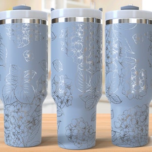 Könnte beinhalten: Drei Edelstahl-Reisebecher mit hellblauer Oberfläche und silbernem Blumendesign. Die Becher haben einen Griff und einen Deckel.