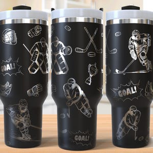 May include: Black stainless steel travel mug with a silver hockey player design. The mug has a handle and says "GOAL!" on the side.