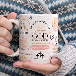 Op de afbeelding: Witte keramische koffiemok met een roze en gouden ontwerp. De mok heeft de tekst "Trust in His Promises", "Christ Lives in Me", "God is My Anchor", "Feeling Blessed", "Pray Believe Receive" en "Savior and King".