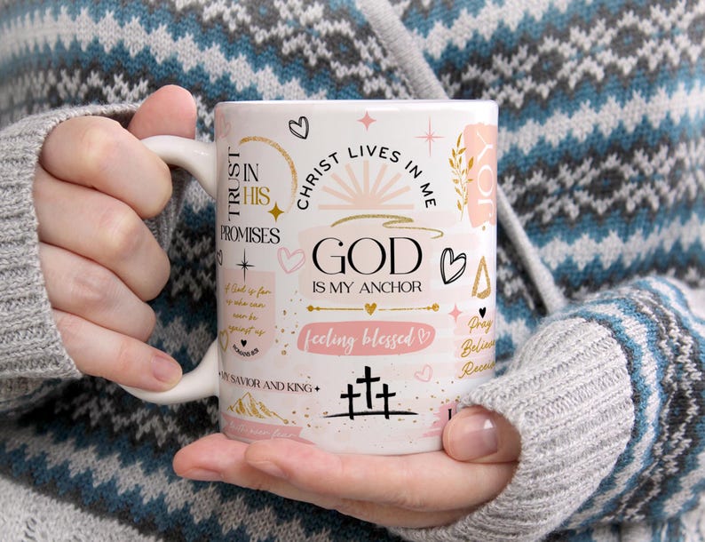 Op de afbeelding: Witte keramische koffiemok met een roze en gouden ontwerp. De mok heeft de tekst "Trust in His Promises", "Christ Lives in Me", "God is My Anchor", "Feeling Blessed", "Pray Believe Receive" en "Savior and King".