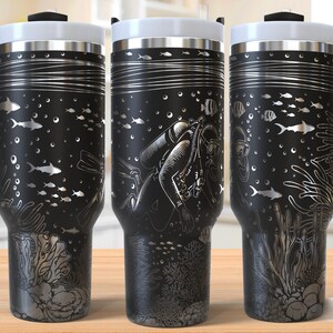 May include: Black travel mugs with white lids and black handles. The mugs have a silver design of fish, coral, and a scuba diver. The words "SEAMLESS DESIGN" are printed on the bottom right of the image.