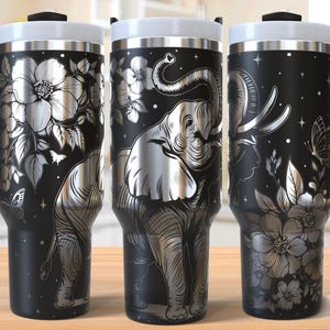 May include: Three black travel mugs with a silver elephant and floral design. Each mug has a black handle, a white lid, and the words "SEAMLESS DESIGN" at the bottom right. The design includes butterflies and stars.