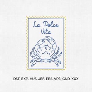 May include: A blue and gold embroidered design featuring a crab illustration and the text "La Dolce Vita" in a stamp-like frame. The design is on a white background. The text is in a cursive font.