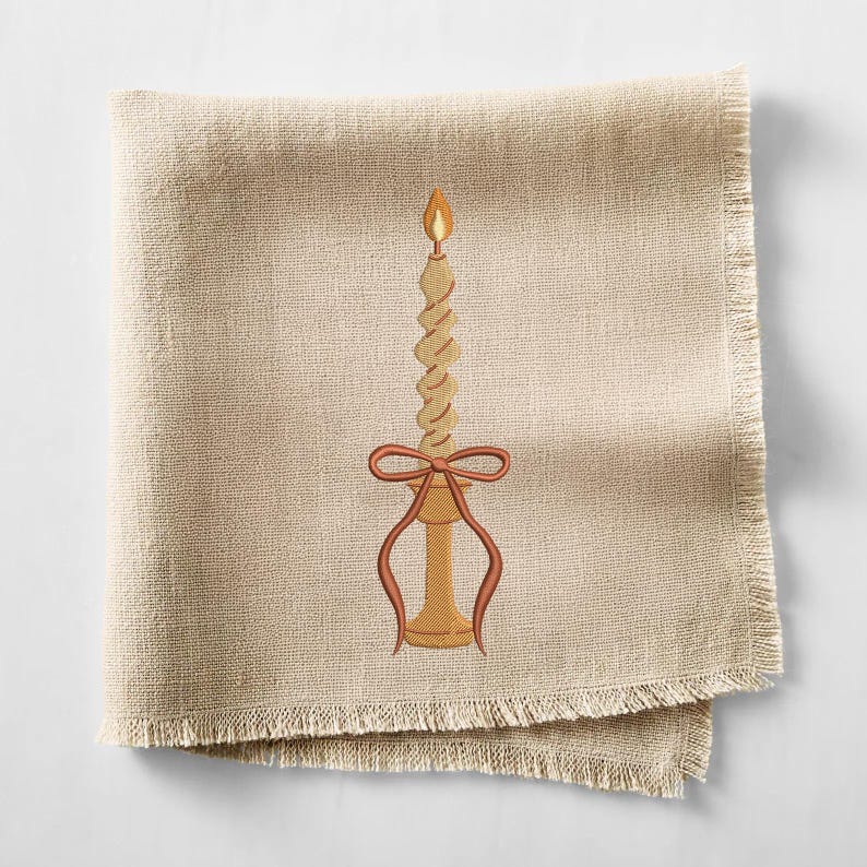 May include: A beige linen napkin with a fringed edge. An embroidered candle design features a twisted candle with a flame, a bow, and a candle holder in shades of brown and orange.