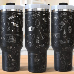 Op de afbeelding: Drie zwarte reisbekers met witte deksels en zwarte handvatten. De bekers zijn versierd met een zilverkleurig nail art-ontwerp. Het ontwerp omvat nagellakflesjes, nagelvijlen en handen die een manicure krijgen. De woorden "SEAMLESS DESIGN" staan in de rechter benedenhoek.