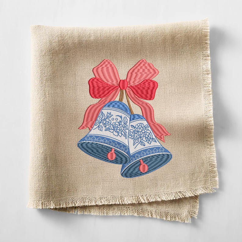 May include: A square beige linen napkin with frayed edges featuring an embroidered design of two blue and white bells decorated with floral patterns, tied together with a large, vibrant red bow with detailed stitching and shading.