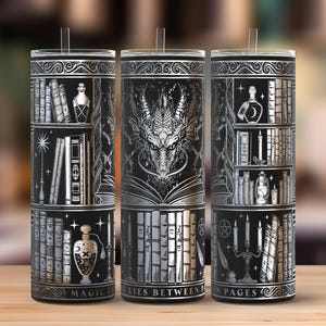 May include: Three black and silver insulated tumblers with a fantasy theme. Each tumbler features a different design: a bookshelf, a dragon, and a bookshelf with candles. The text "MAGIC LIES BETWEEN PAGES" is printed on the bottom.